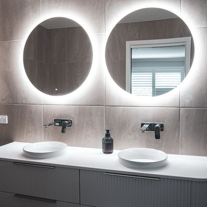 Modern bathroom vanity with two round backlit mirrors, dual sinks, and dark faucets.