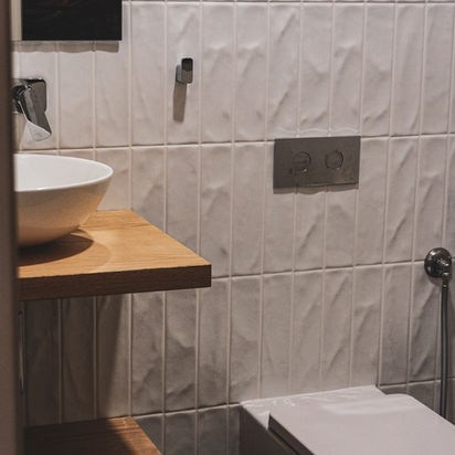 Modern bathroom with white textured tiles, wooden counter, sink, and toilet.