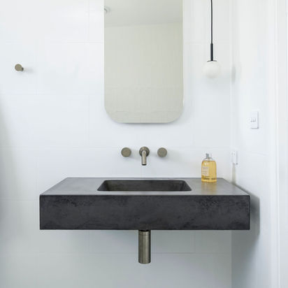 Elegant floating dark concrete sink, rounded mirror, and pendant light.