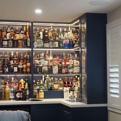 Built-in home bar with liquor bottles, illuminated dark blue shelves.