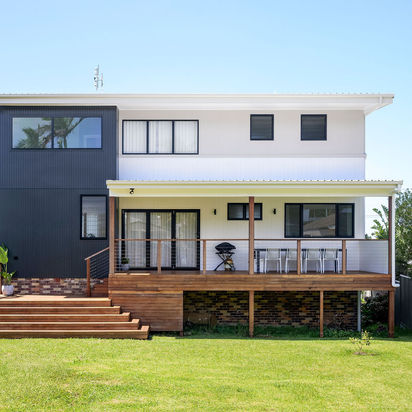 Modern two-story house with a spacious wooden deck and green lawn.