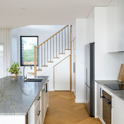 Modern kitchen with large island, dark appliances, and wooden staircase.