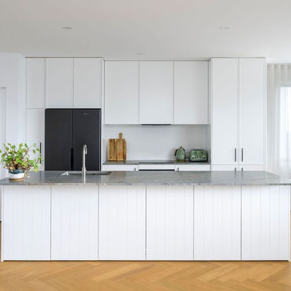 Modern white kitchen with large island, black fridge, and wooden floor.