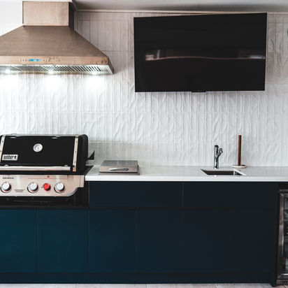Modern outdoor kitchen with grill, sink, television, and mini-fridge.