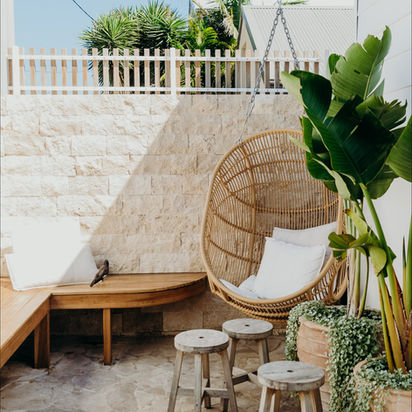 Stylish outdoor patio with hanging rattan chair, wooden bench, and potted plants.