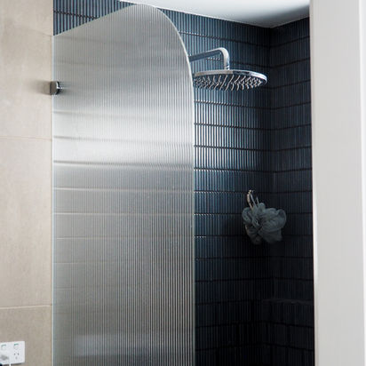 Modern shower with curved metal screen, dark tile wall, rainfall showerhead.