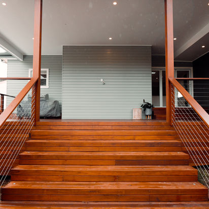 Polished wooden stairs leading to a modern house's covered outdoor deck.